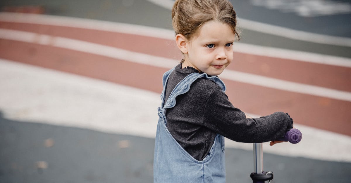 Balance overly sweet liqueurs - Side view of adorable preschool girl in casual clothes riding scooter on asphalt ground and looking away