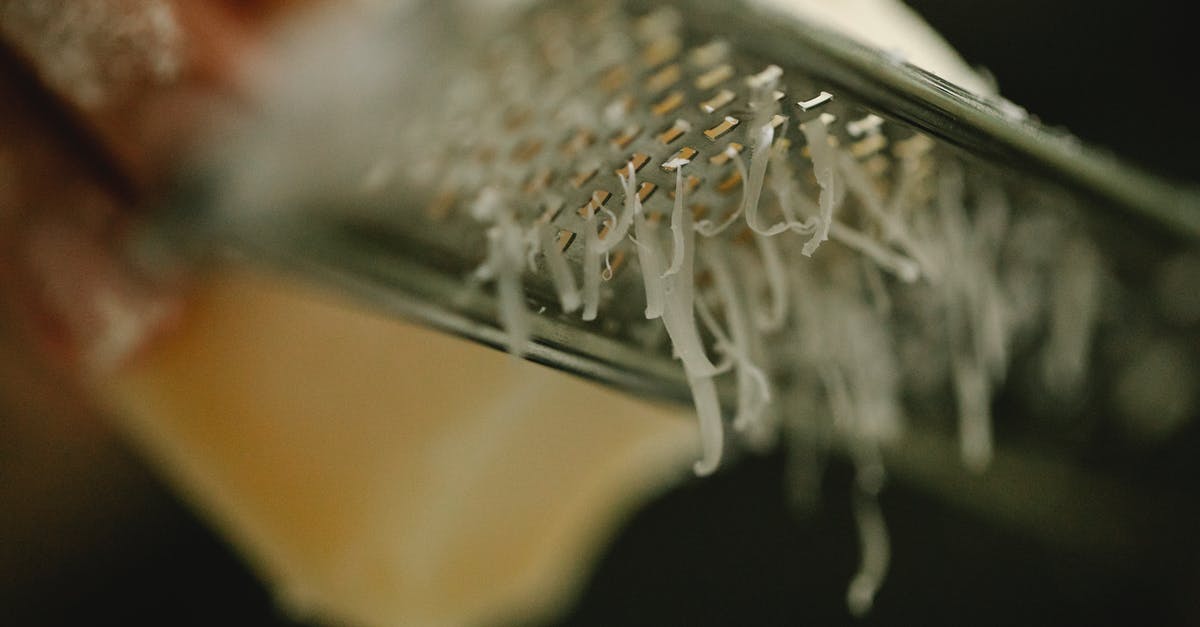 Balancing out a good souffle and burnt cheese on top - Crop unrecognizable chef grating delicious cheese on narrow stainless grater in dark kitchen