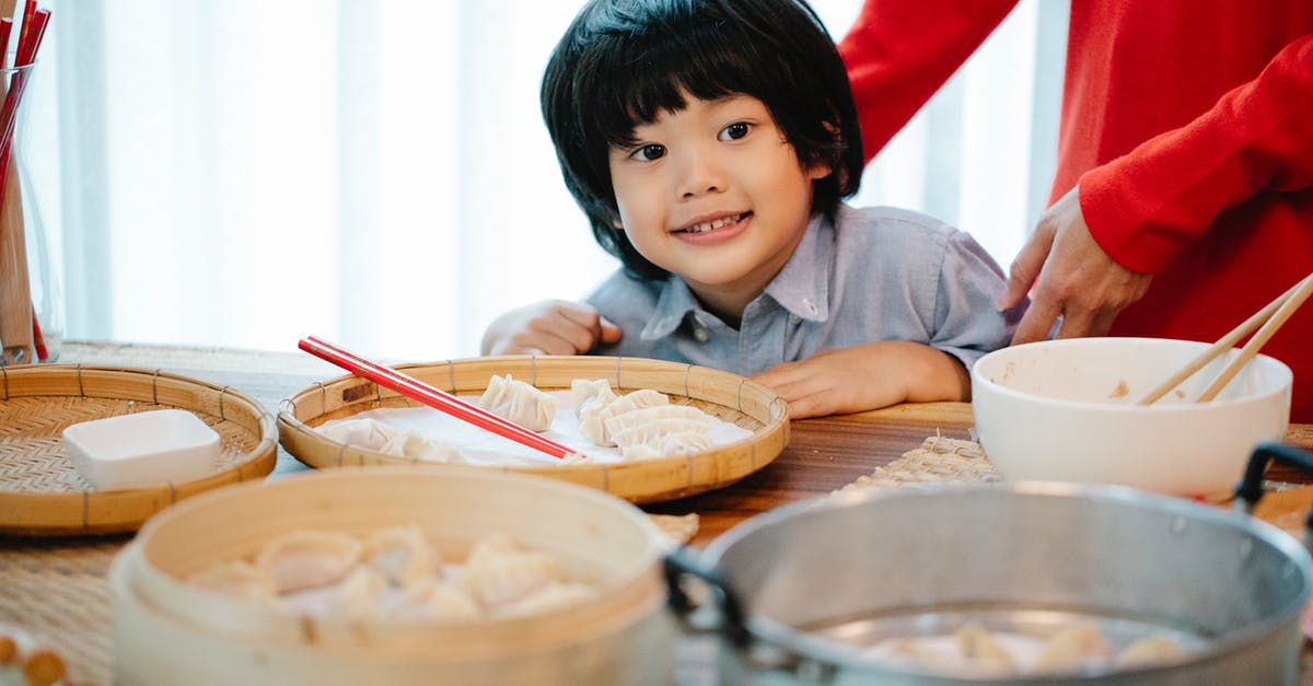 Bamboo Steamer VS Normal Steamer - Positive ethnic boy sitting at table with homemade Chinese dumplings on bamboo plates for steamer