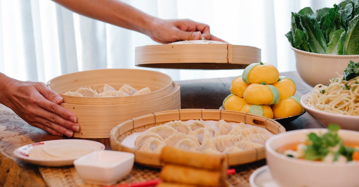 Bamboo Steamer VS Normal Steamer - Crop unrecognizable female standing at table with various Chinese dishes and uncooked jiaozi dumplings in bamboo steamer