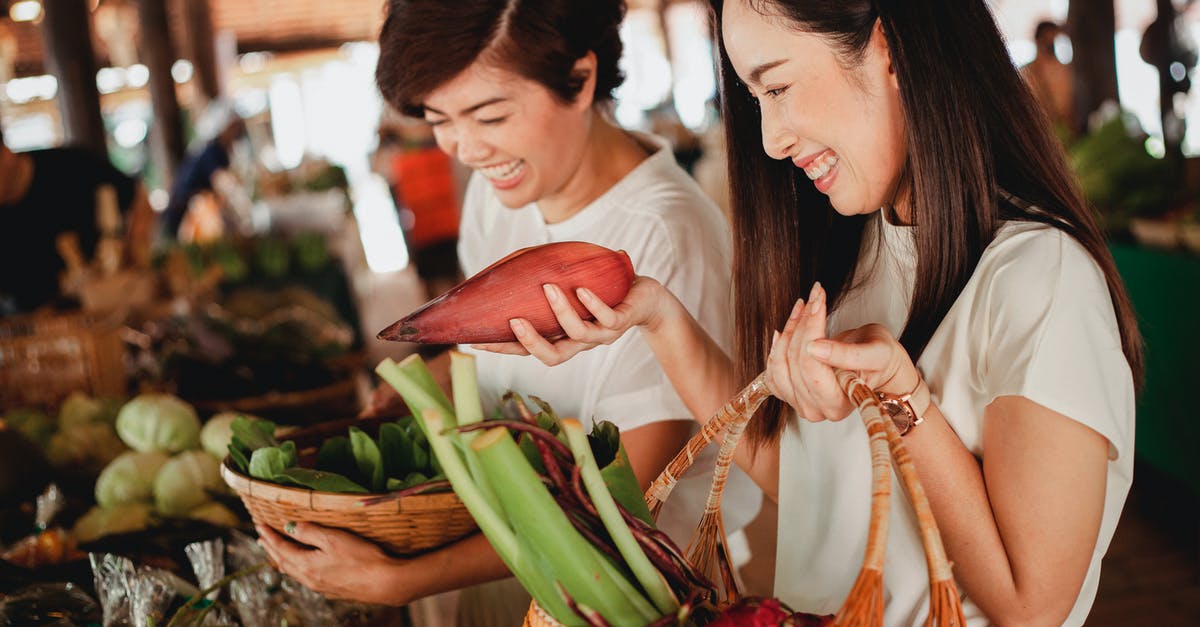 Banana blossoms versus bean sprouts - Crop Asian woman with banana flower near girlfriend in bazaar