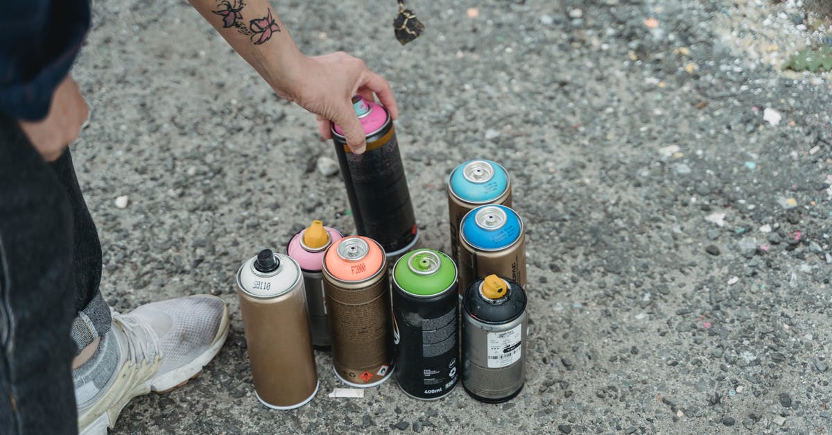 Bananas - too many - so how can I preserve them? - Crop anonymous person in sneakers with tattoo and heap of multicolored spray paint cans on ground standing on street in city