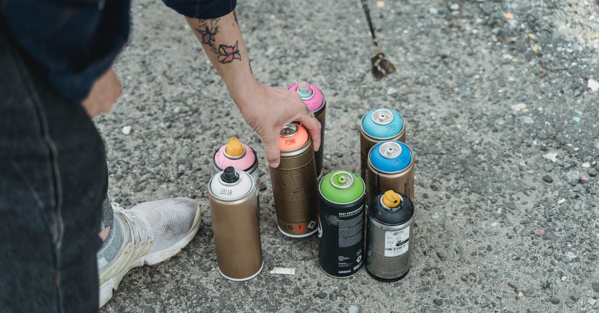 Bananas - too many - so how can I preserve them? - Crop faceless tattooed artist taking paint bottle from heap of multicolored spray cans placed on ground on street of city