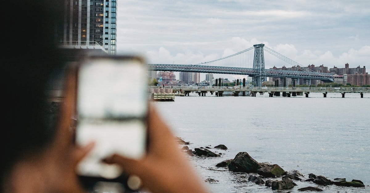 Bay used to crisp fermenting pickles - Crop anonymous African American male standing on embankment and taking picture of skyscrapers and bridge