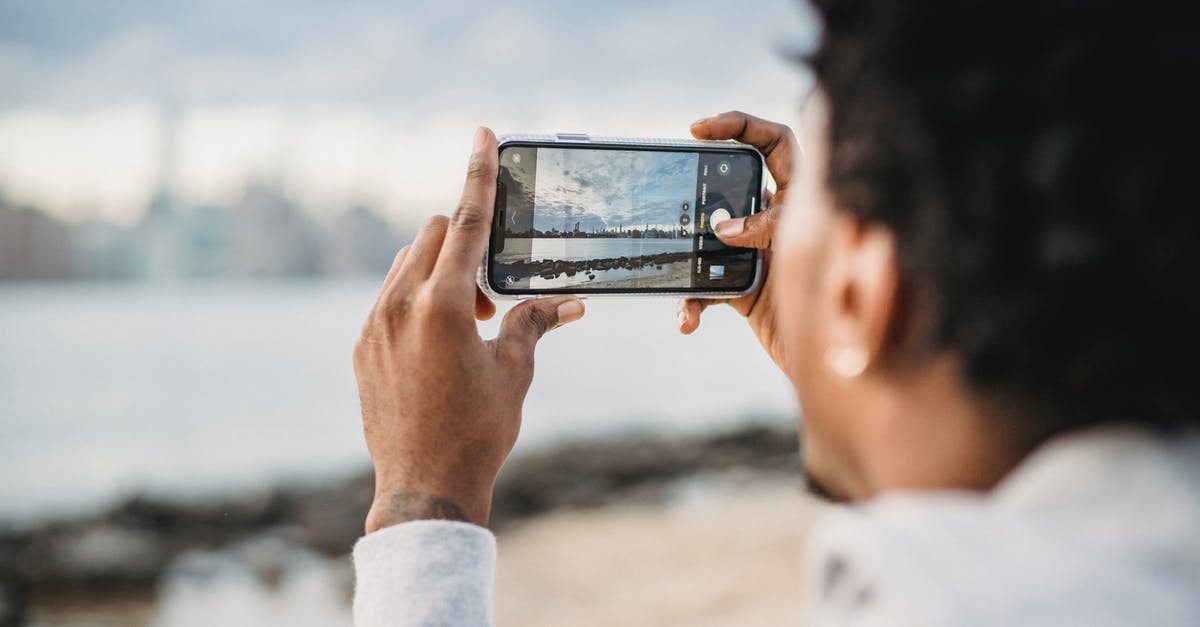 Bay used to crisp fermenting pickles - Back view of crop African American male taking picture on mobile phone of coastal city located on river bank