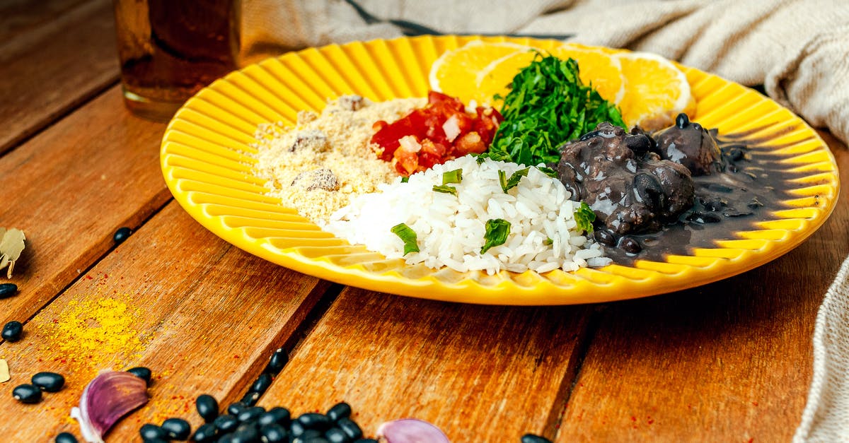 Bean based stew. Alternative to tomatoe sauce - Appetizing traditional Brazilian Feijoada dish of black bean stew served with boiled rice and couscous served on wooden table and decorated with black beans and garlic cloves