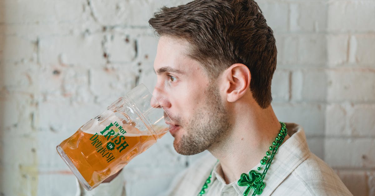 Beer Battered Onion Rings -- what makes them look shiny? - Side view of young male drinking glass of beer on festive event near white brick wall