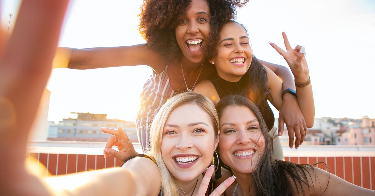 Best moment to put salt in spaghetti? - Cheerful young diverse women showing V sign while taking selfie on rooftop