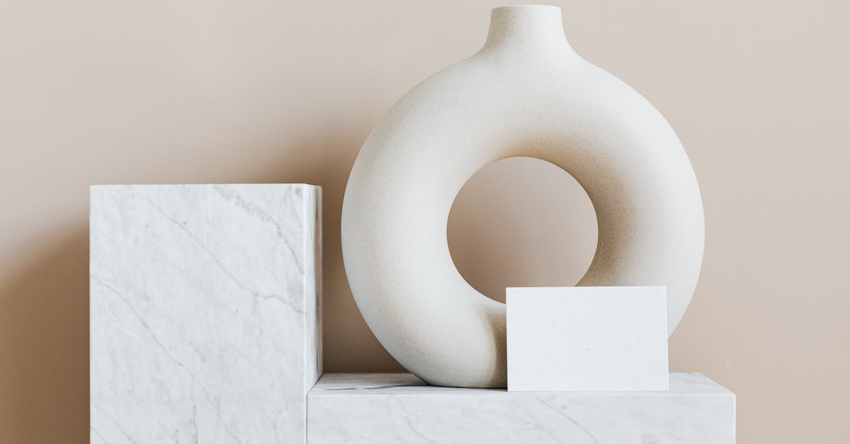 Best vessel for frying - Composition of creative white ceramic vase in ring shape with empty postcard placed on white marble shelf against beige wall as home decoration elements or art objects