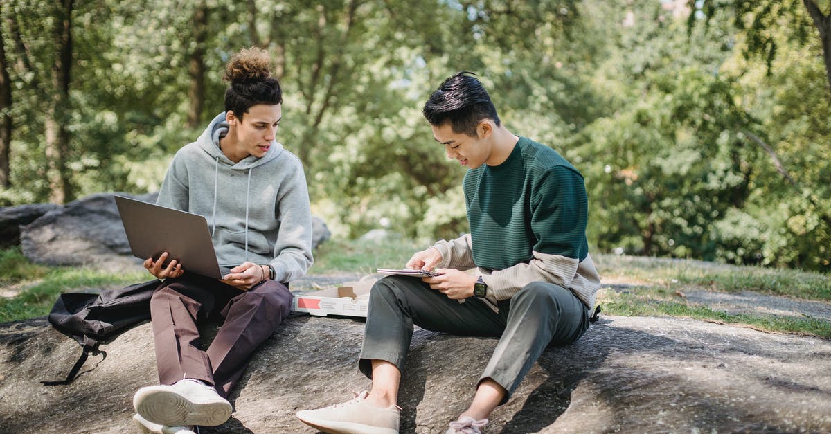 Best way to reheat pizza - Full body young men in casual clothes spending time on ground with netbook and pizza while taking notes in notebook in summer sunny day with trees on background