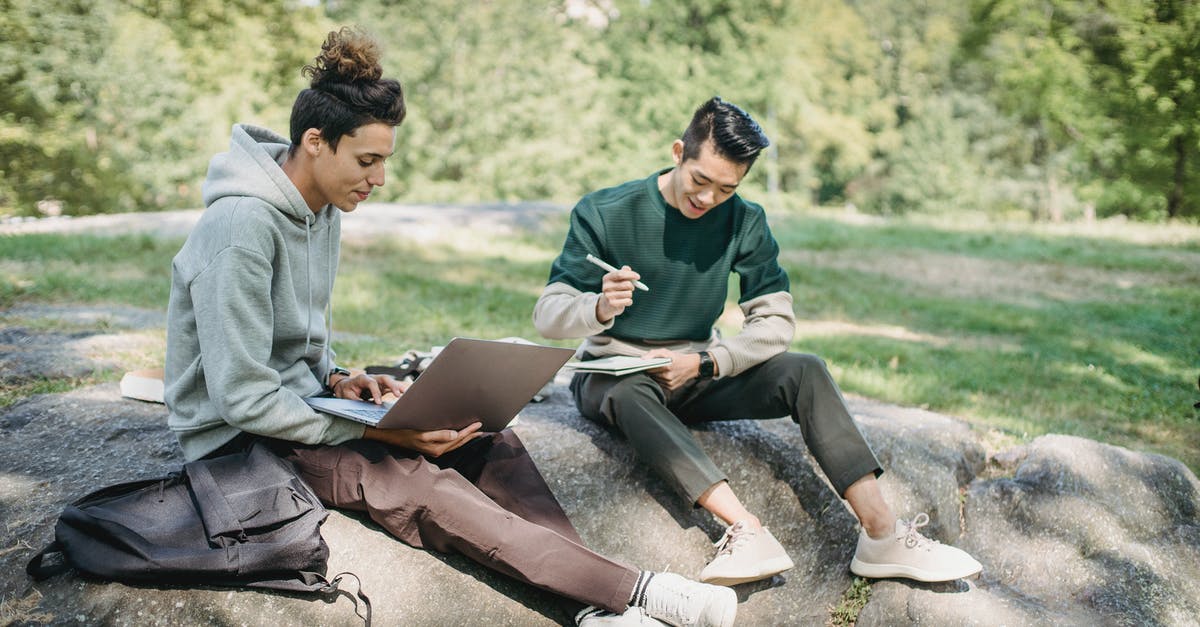 Best way to reheat pizza - Full length young men friends in casual outfit sitting on big boulder with computer while writing notes with pen in notepad in summer sunny day with trees on background