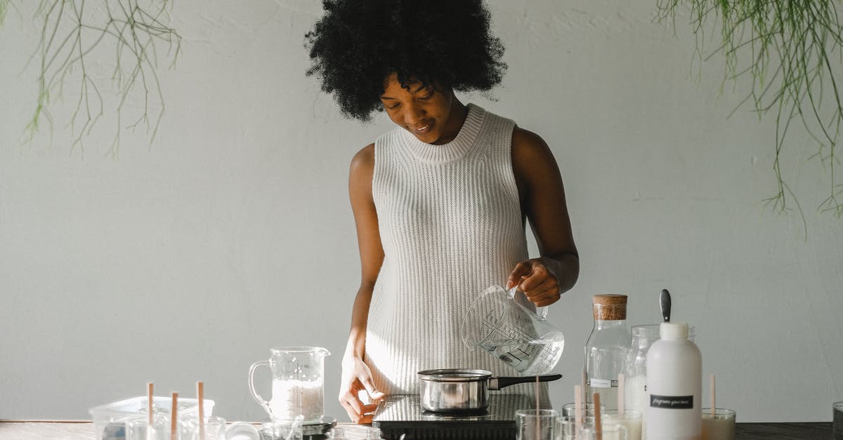 Bircher muesli: how to make oats soak liquid - Positive African American female artisan pouring liquid in pot while making wax for candles in pot on cooker