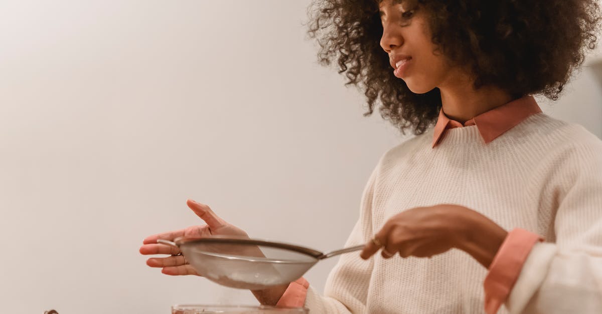 Biscotti with chocolate drizzle in batter - Side view of African American female cook with sieve pouring flour into bowl with chocolate batter while cooking in kitchen