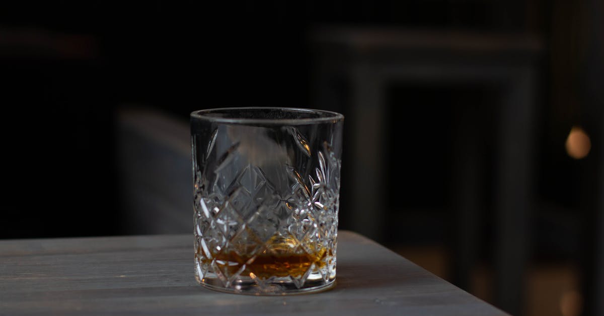 Bitter taste of rocket pesto - Cut glass with aromatic cognac on bottom placed on wooden table in dark living room