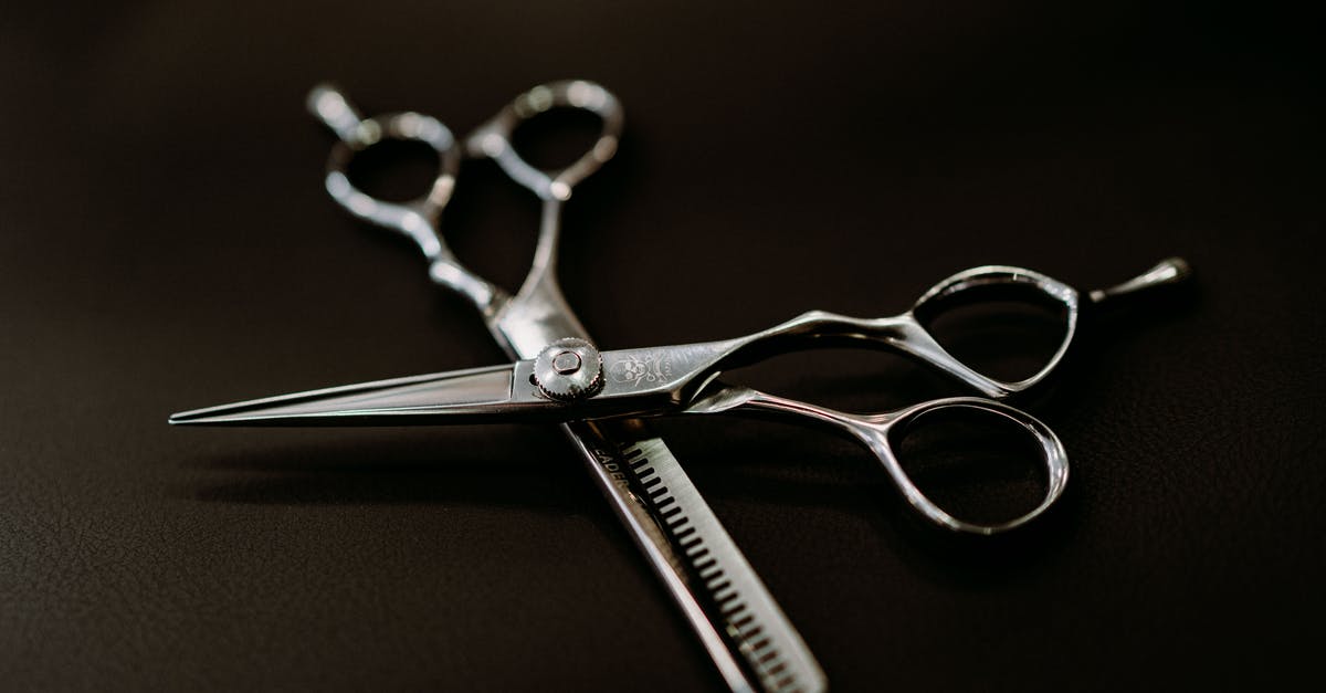 Black flakes from new cast iron pan - From above of shiny steel scissors for hairdresser on black background of studio