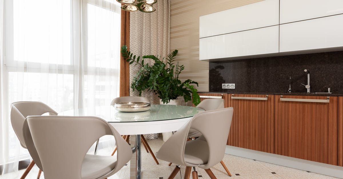 Black spots in the kitchen sink - Plate on white round table with stools placed on tiled floor near green potted plant and counter with sink and wooden cupboards in dining room