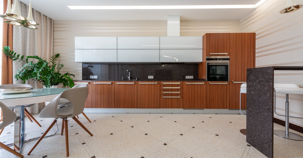 Black spots in the kitchen sink - Contemporary kitchen with modern appliance and black counter with wooden cupboards placed near table with chairs and green potted plant on tiled floor