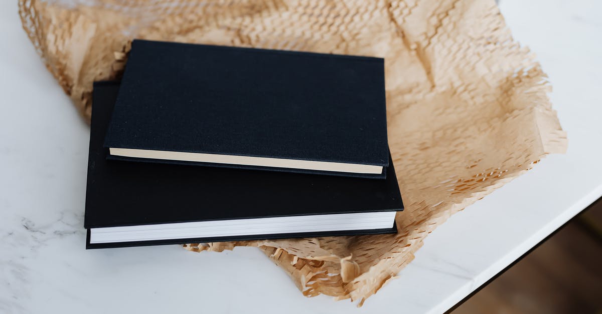 Black spots while ripening store brought mangoes by paper [duplicate] - From above of notebook pair with black empty hardcover placed with packing paper and white marble table during prepare for postal delivery