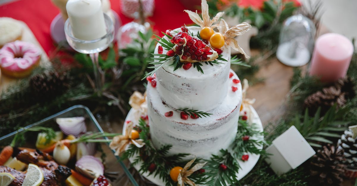 blackened carrot cake - High angle of table served with white Christmas cake decorated with garnet and physalis near leaves and branches with cones near candles and turkey with lemon and onion near donuts