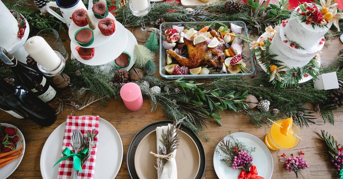 blackened carrot cake - From above of Christmas table served with cake and plates with napkins and drink with flowers and twigs near candles and donuts near turkey with lemon and alcohol bottles