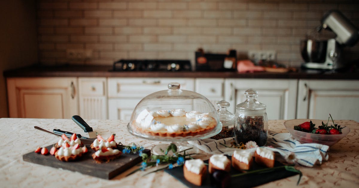 Blender vs food processor vs juicer - Appetizing sweet cake and desserts decorated with cream and strawberries placed on table near white cabinets in kitchen