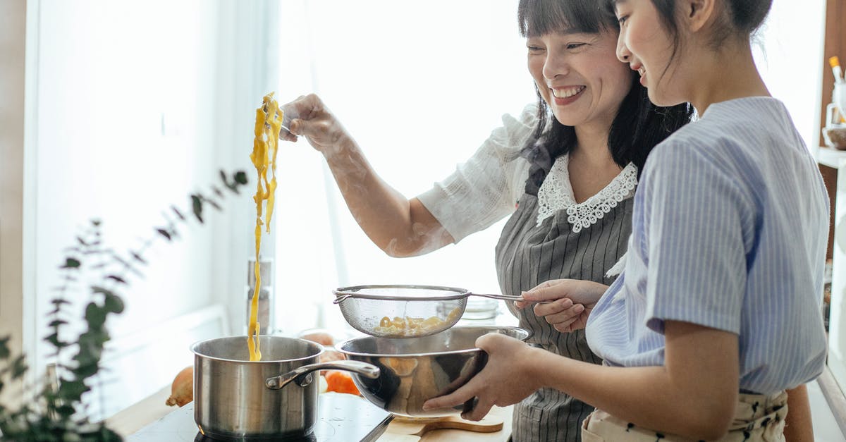 Boiling rice - drain or boil off water? - Side view of smiling Asian teenager with middle age mother serving hot boiled pasta in drainer