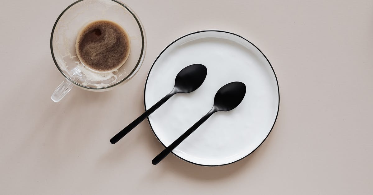 Bold Setting on Coffee Maker - From above composition of ceramic plate with black spoons placed near glass cup of coffee on beige table