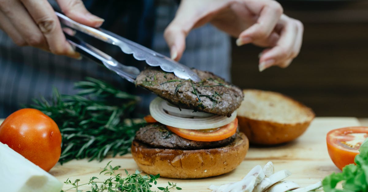 Bolognese: can I add the meat after tomatoes? - Unrecognizable female cook using tongs to put juicy meat on bun with onion and slice of tomato while making burger against blurred background