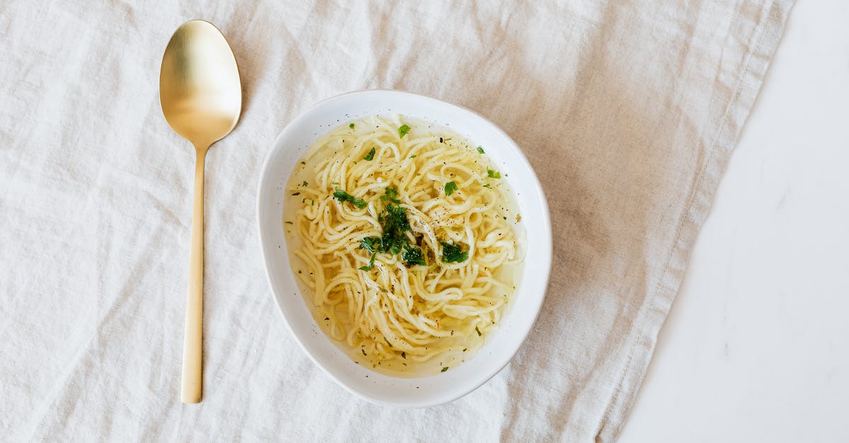 Bone broth has green tint; is this normal? - Top view of bowl with yummy noodle soup with greens and golden spoon placed on rumpled linen cloth on marble table