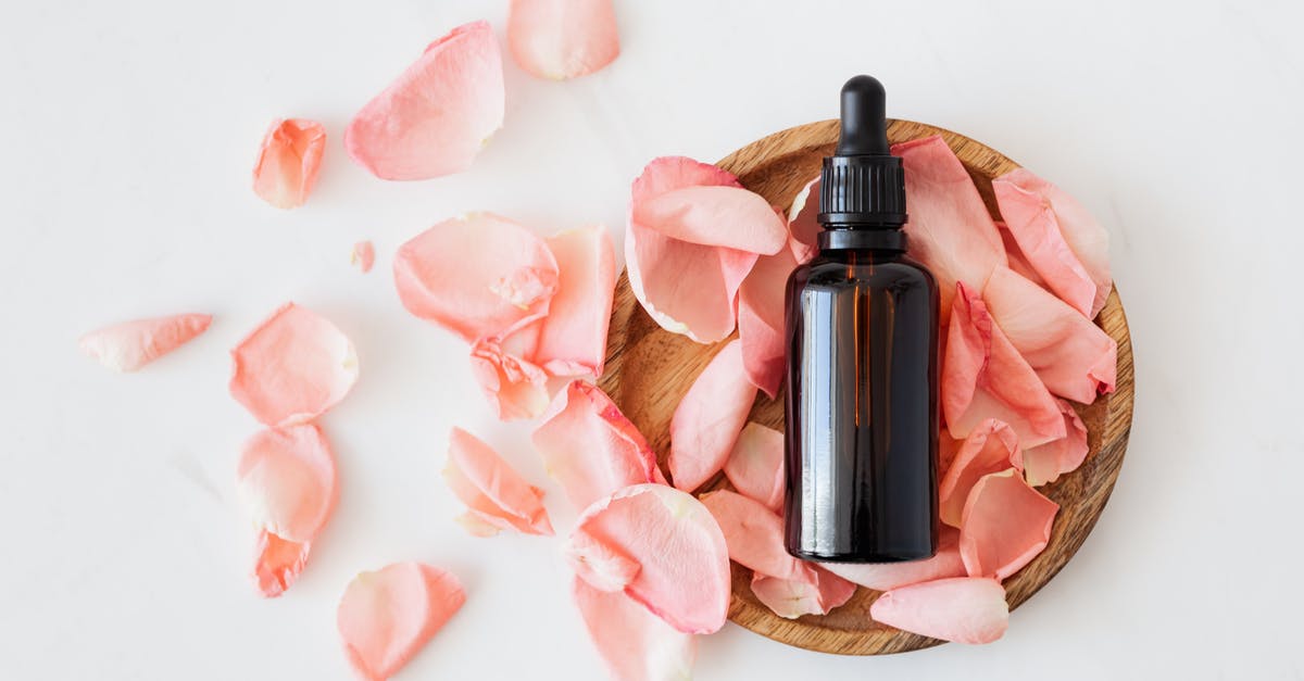 Bottled coconut oil - Top view of empty brown bottle for skin care product placed on wooden plate with fresh pink rose petals on white background isolated