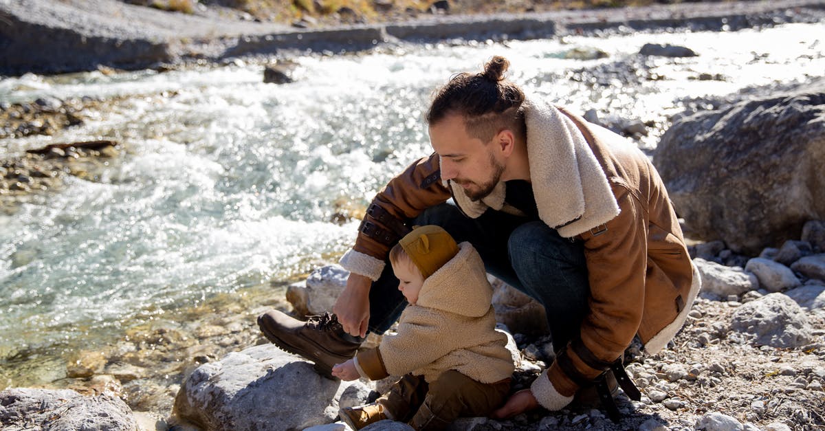 Bread Proving Time in Warm Climates - Bearded young father with little child in casual warm clothes sitting on rocky ground near river and enjoying time together while weekend