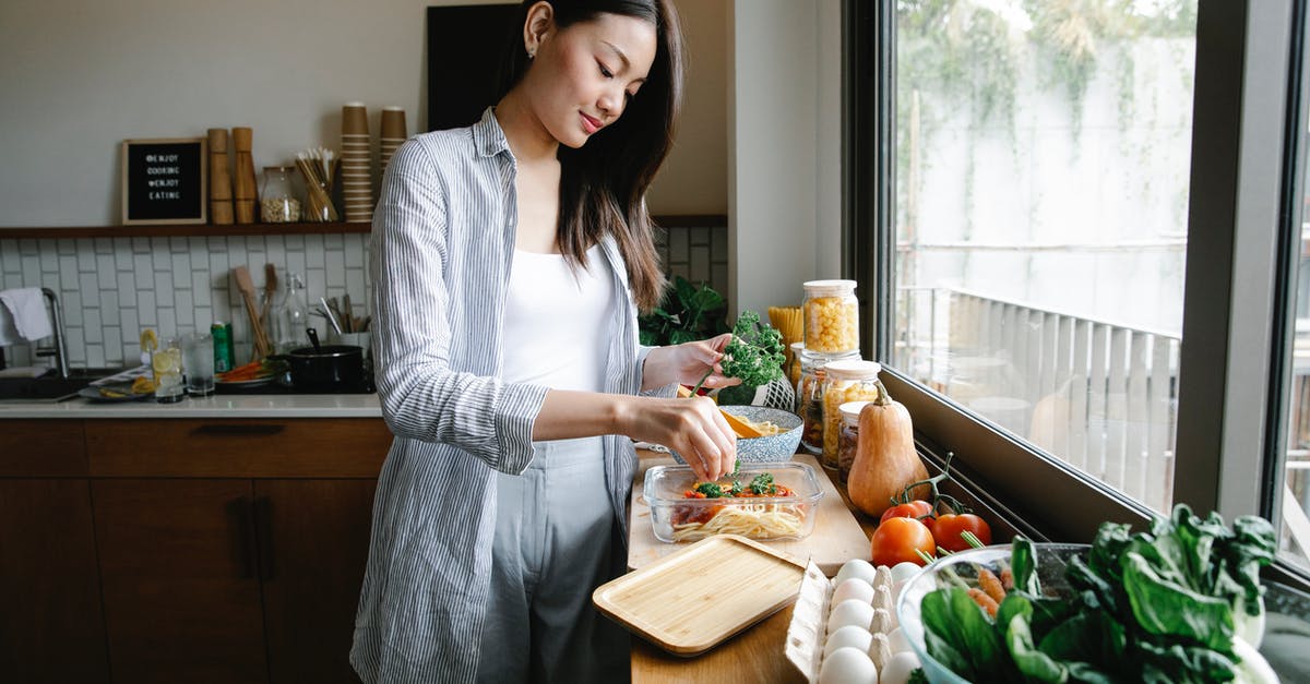 Brewed vs regular soy sauce : phytochemical content - Side view of Asian female adding fresh parsley into glass container with pasta and bolognese sauce while cooking in kitchen with various products and kitchenware