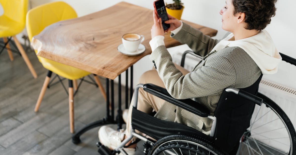 Brewing coffee concentrate using both hot and cold methods - Freezing concentrate - Side view full body of female in wheelchair taking picture of hot coffee while sitting at wooden table in cafeteria