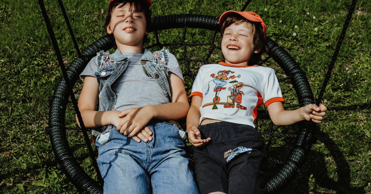 Buckwheat groats have grassy smell? - From above of happy boys with closed eyes wearing caps lying on round swing on grassy lawn while having fun in yard