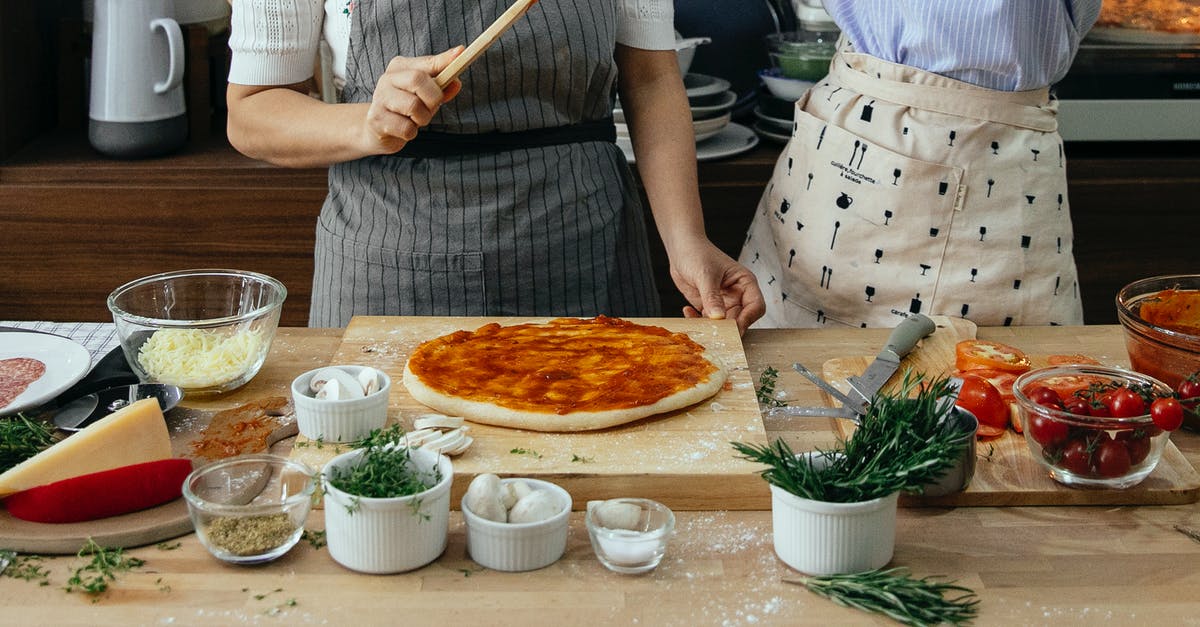 Buckwheat raw pizza base - Crop anonymous female cooks at table with tomato salsa on raw dough near assorted ingredients for pizza in house