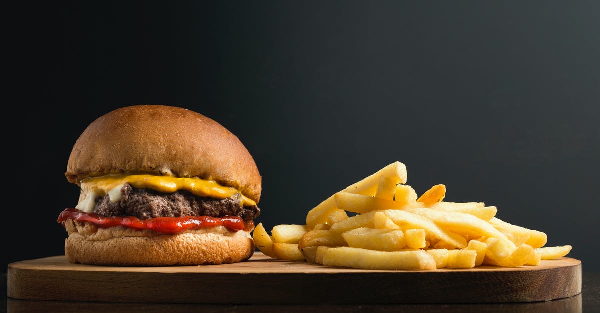 Burger without patty? - Appetizing burger with meat patty ketchup and cheese placed on wooden table with crispy french fries against black background