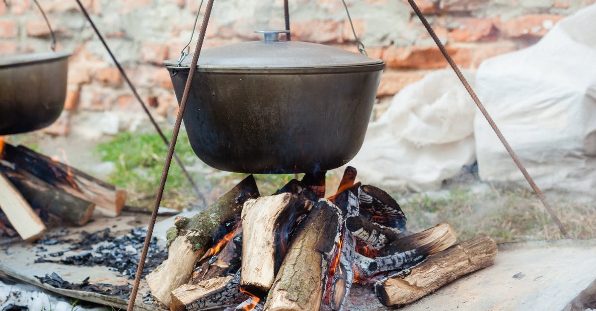 Burned enameled cast iron stock pot - Metal pots hanging over burning cut tree trunks on metal sheet in daytime on blurred background