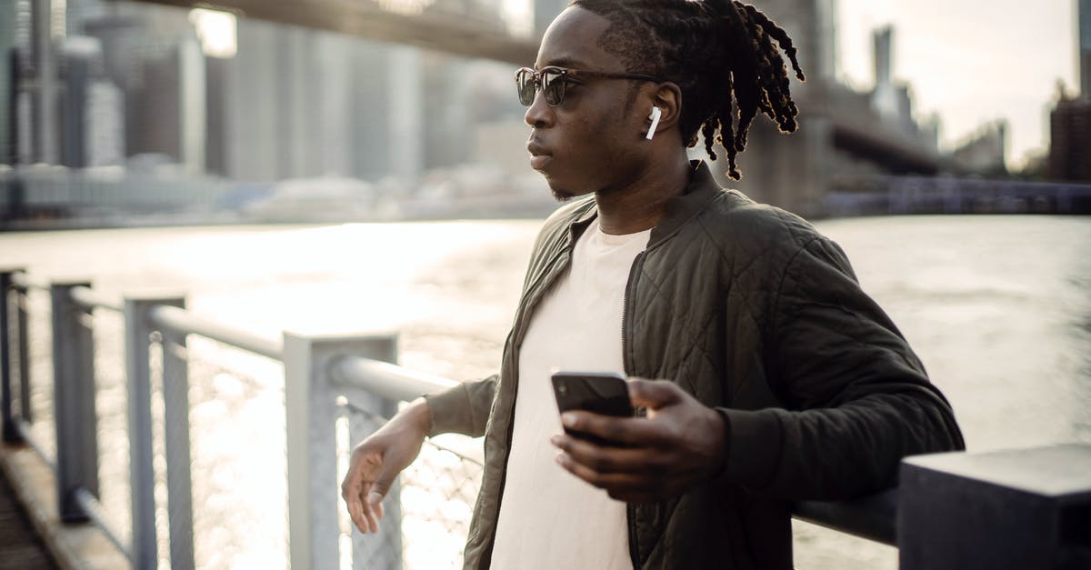 Burned water out of pot...popping sound a month later? - Thoughtful masculine African American guy in sunglasses and true wireless earphones listening to music from cellphone while standing leaned on bridge fence passing over city river