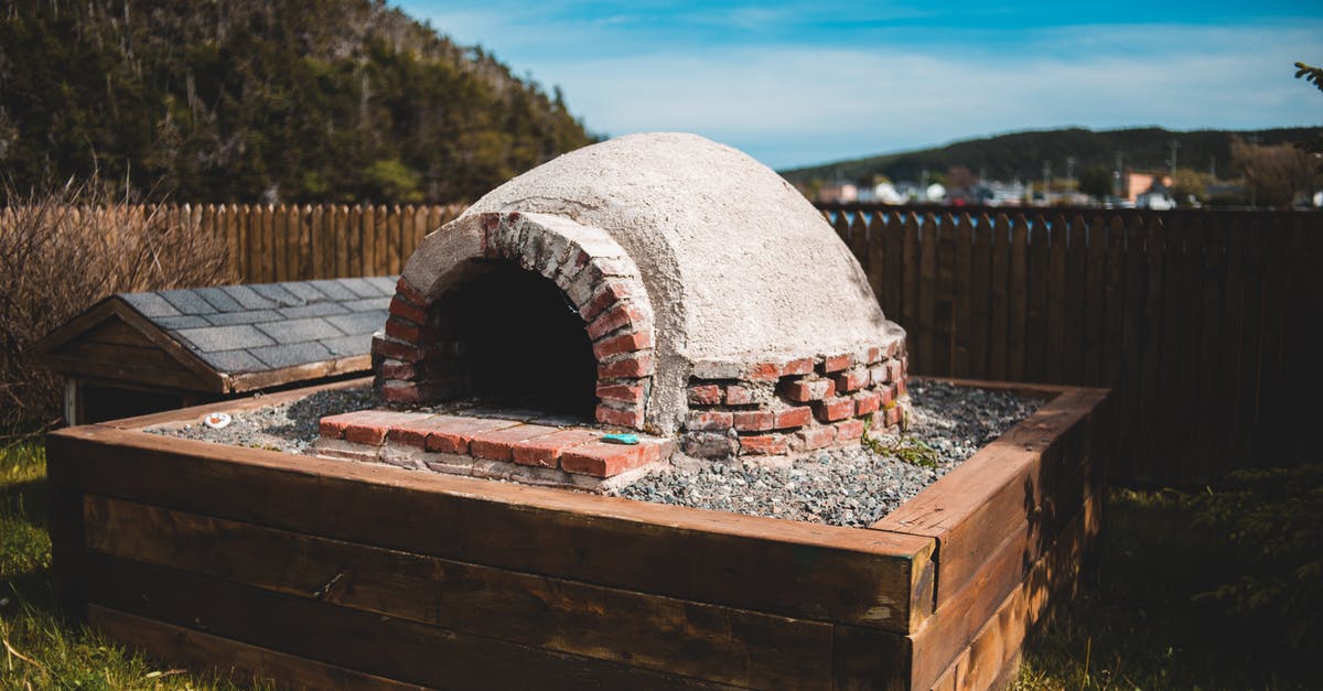 Burnt corneal in my wood pellet (Uuni) pizza oven - Aged outdoor pizza oven on wooden construction on grass behind mountains under blue cloudy sky