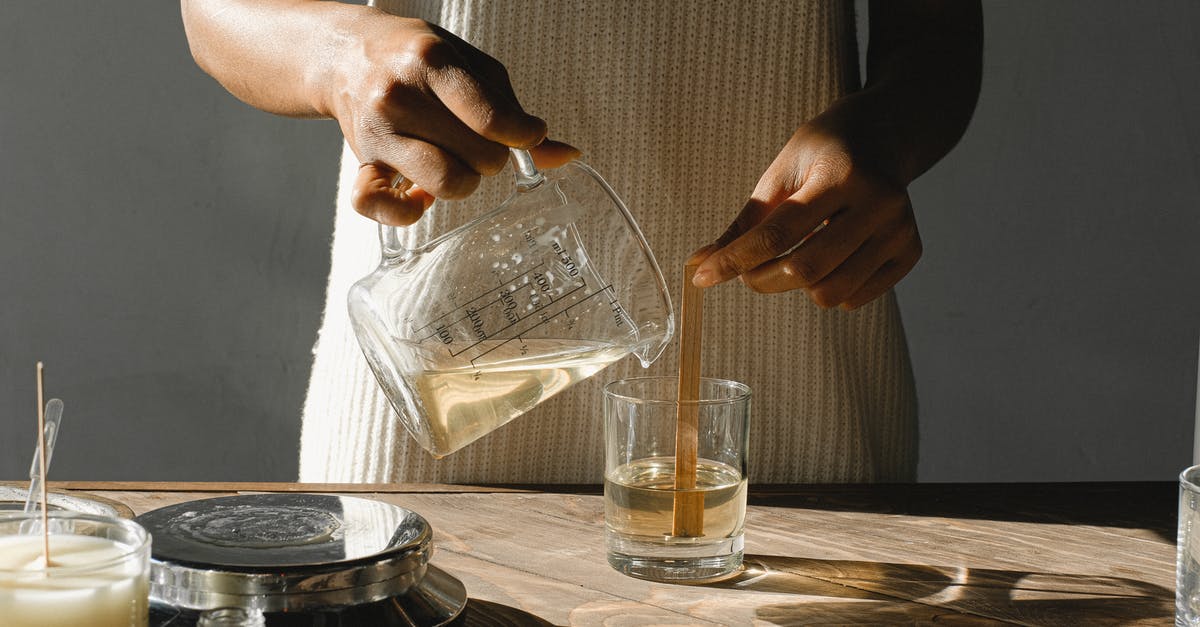 Butter melted then soften - Unrecognizable African American female pouring melted wax from beaker into glass mold with wooden wick while making candles at table