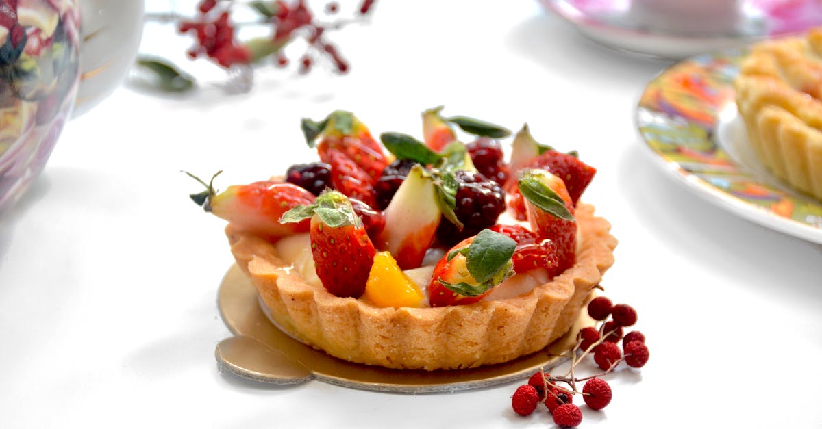 Butterscotch Pie setting - Tasty tarlet decorated with ripe strawberries on table with fresh berries near tea set on blurred background in light kitchen