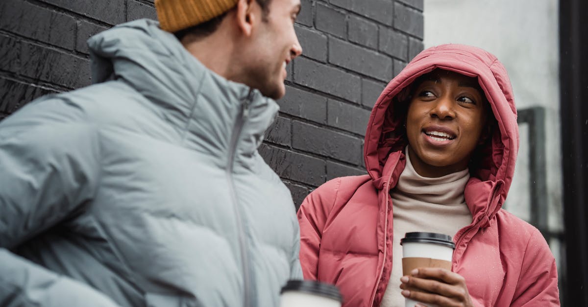Caffeine content of cold-brewed coffee: higher or lower than hot-brewed? - Cheerful multiracial couple in warm outerwear with takeaway hot beverages looking at each other while standing on street in overcast weather