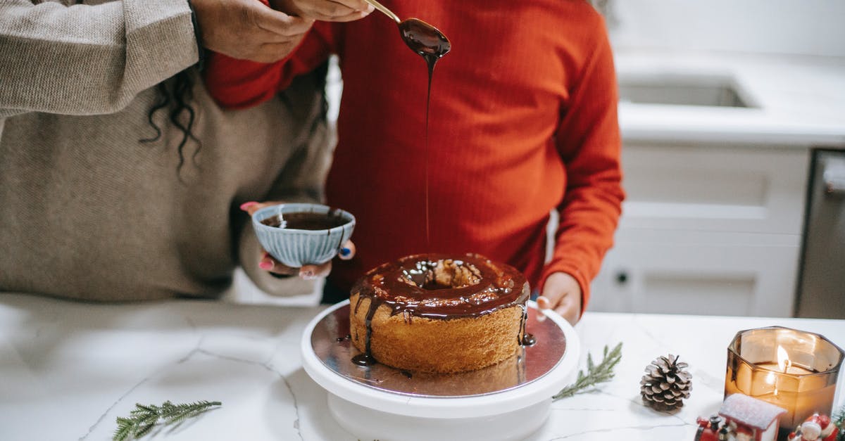 Cake help urgent! - Crop unrecognizable woman helping ethnic daughter decorating sweet sponge cake with chocolate glaze while preparing for New Year holiday