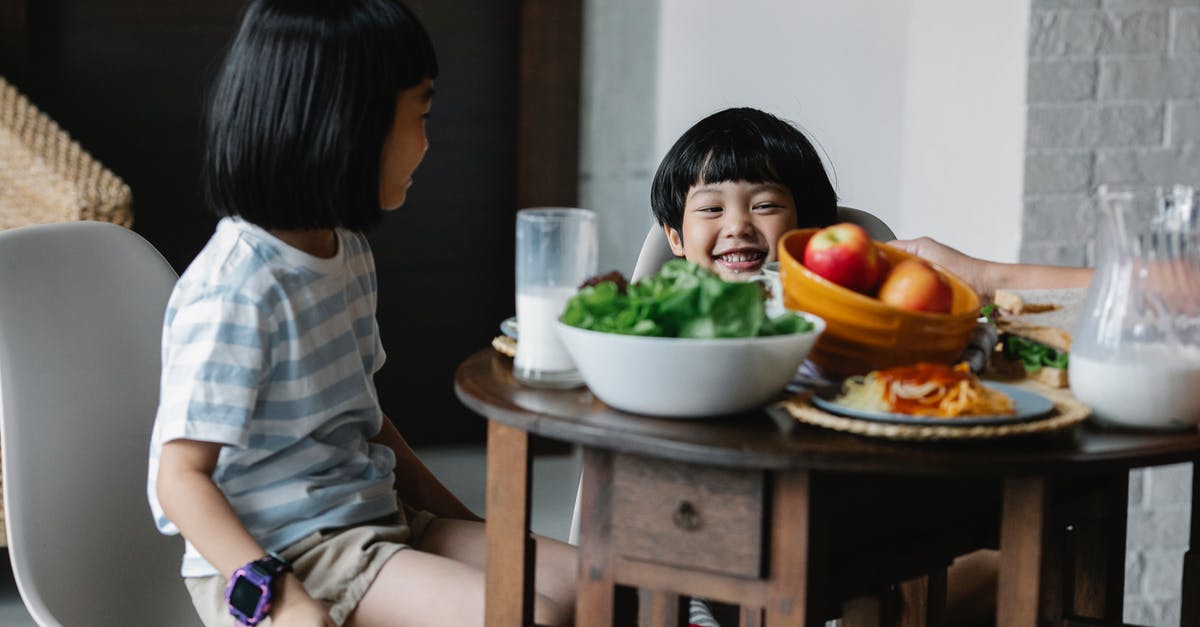 Calcium chloride as substitute for sodium chloride - Cheerful Asian boy and girl sitting at served table with bowl of fruits and jug of milk in kitchen in breakfast time