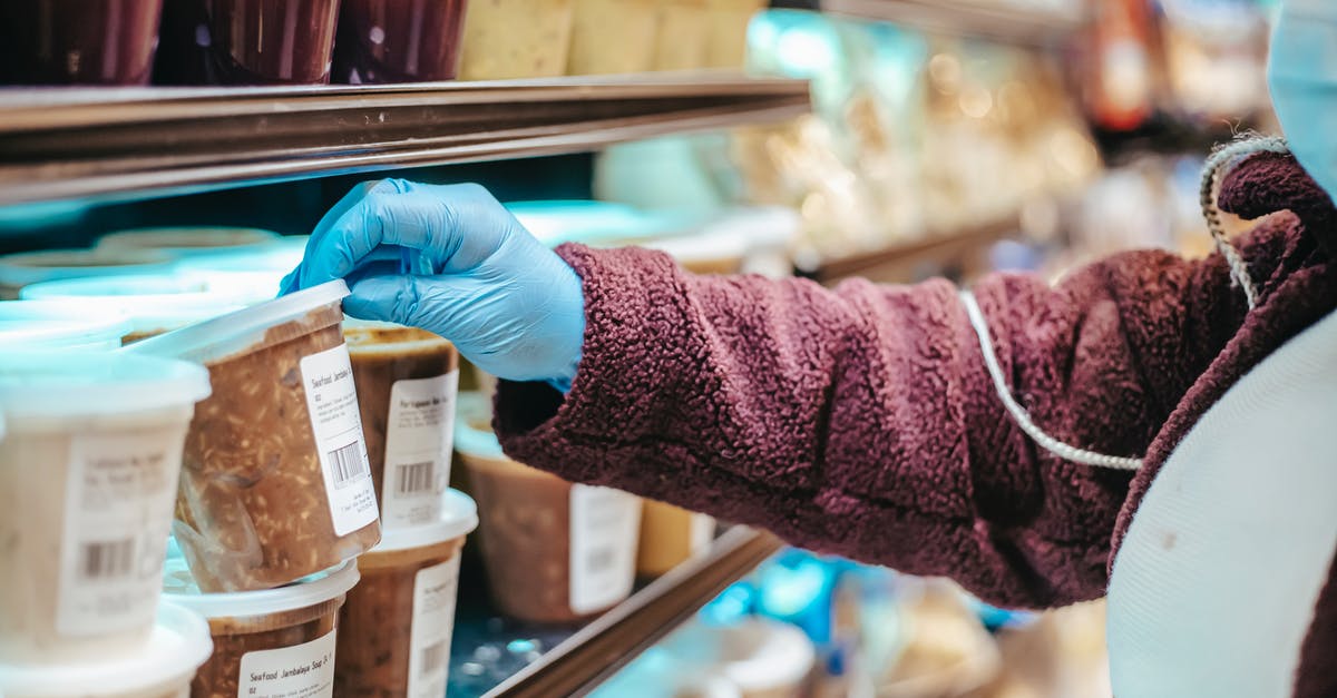 Calculating Nutrition Information for Commercial Food Labeling - Crop anonymous female customer in protective mask reading label on frozen food in plastic container in grocery store