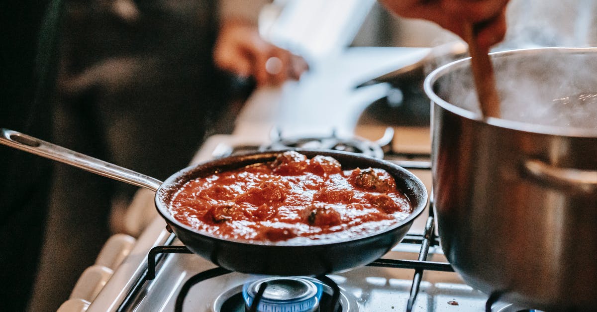Calories in alcohol-based sauce brought to boil (bourbon chicken) - Crop unrecognizable person stirring boiling water in saucepan placed on gas stove near frying pan with appetizing meatballs in tomato sauce