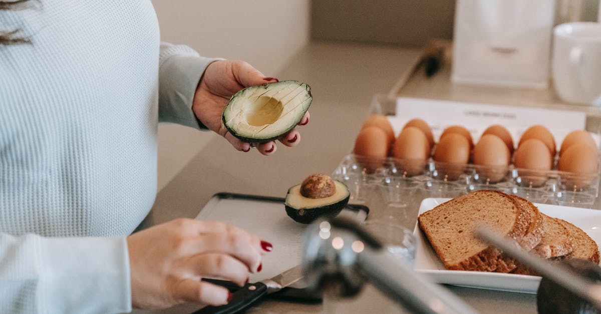 Calories in toast vs bread - Crop faceless female cook preparing avocado while making toasts at table with sliced sliced bread and eggs in kitchen during breakfast