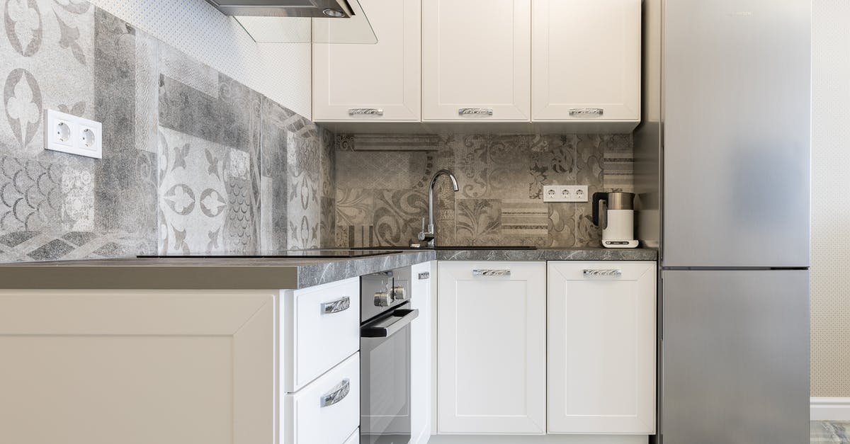Camping stove to supplement an electric hob - Modern kitchen interior with white cabinets and fridge against electric kettle and ornamental wall in light house