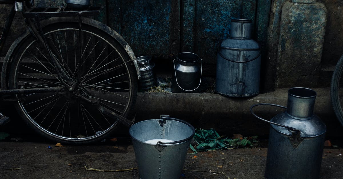 Can a cast-iron casserole be used for steaming? - Tin vessels and metal bucket with milk placed near bike leaned on shabby rusty wall