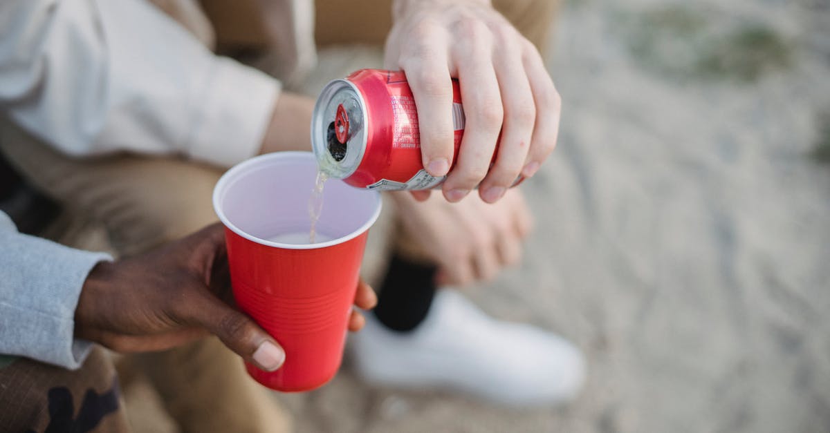 Can beef stew be reheated several times? - From above of crop anonymous man pouring fizzy drink from can into red plastic cup of black friend while sitting on sandy ground